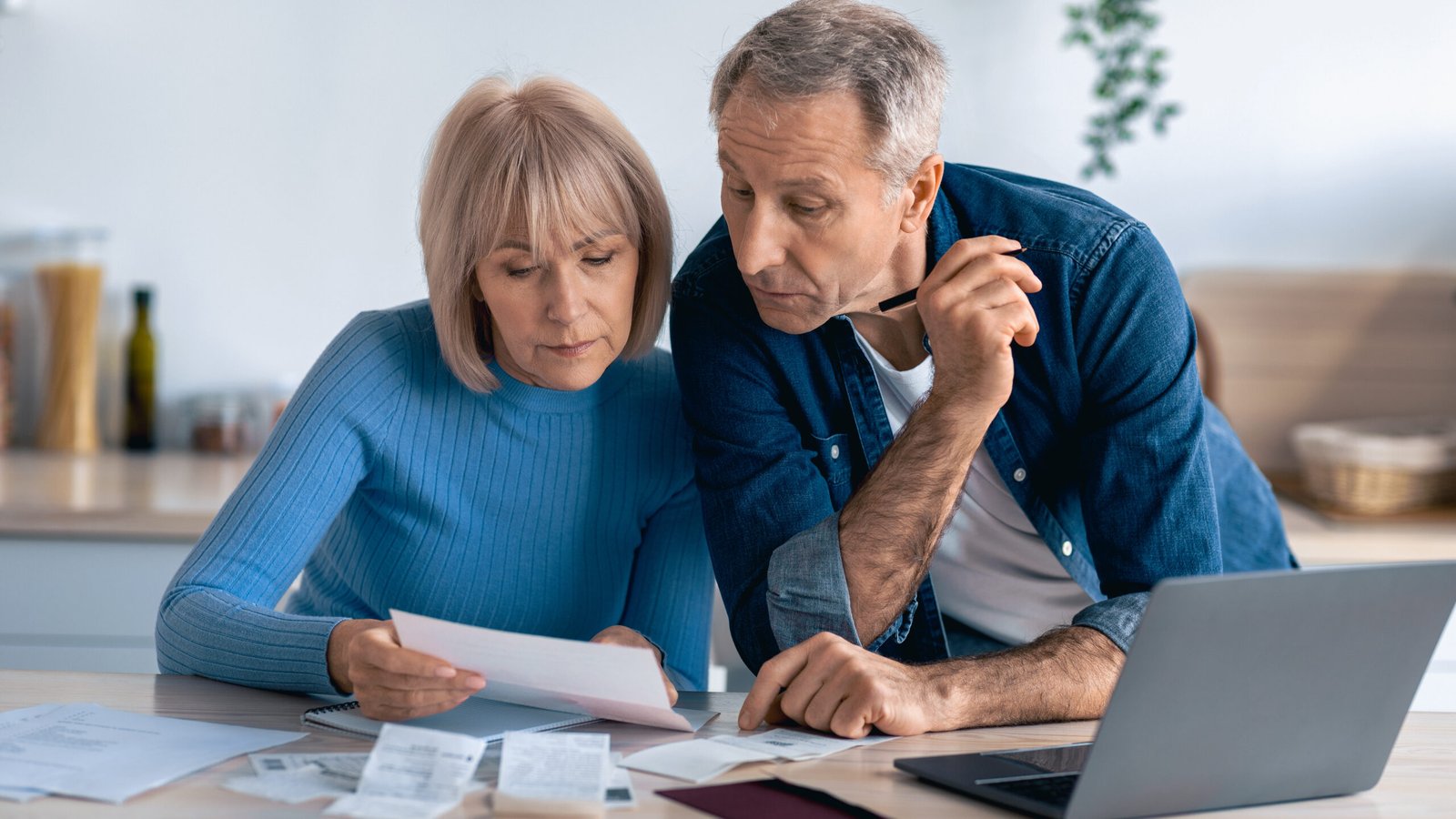 Elderly couple sitting at table using laptop, paying bills